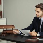 Un professionnel en costume assis à son bureau examine des documents juridiques pour un projet de création entreprise